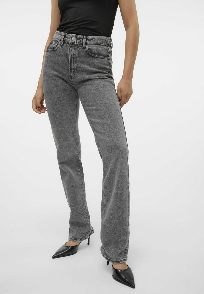 Jean gris taille haute avec une coupe droite, en tissu denim, design à cinq poches et coutures contrastées, associés à des talons noirs elegants.