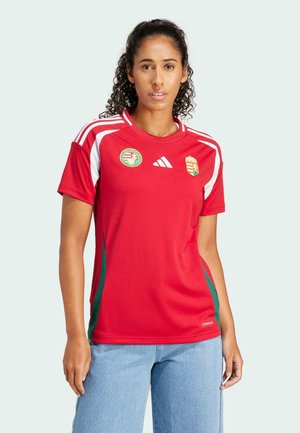 Punainen urheilupaita, jossa on valkoisia yksityiskohtia ja vihreät sivupaneelit, sisältäen Unkarin logon ja Adidasin brändäyksen. Lyhyet hihat ja pyöreä kaula-aukko.