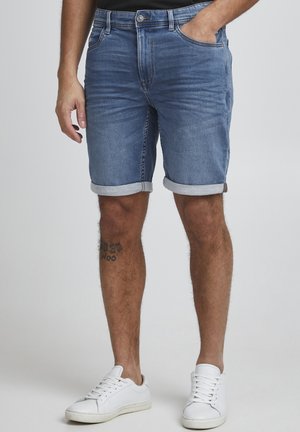 Lys blå denimshorts med oppbrett, fem lommer og sikkerhetsknapp. Sammen med hvite sneakers.