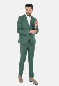 Giacca verde chiaro su misura realizzata in tessuto testurizzato, abbinata a una camicia bianca. Presenta una vestibilità slim e dettagli sottili sui polsini.