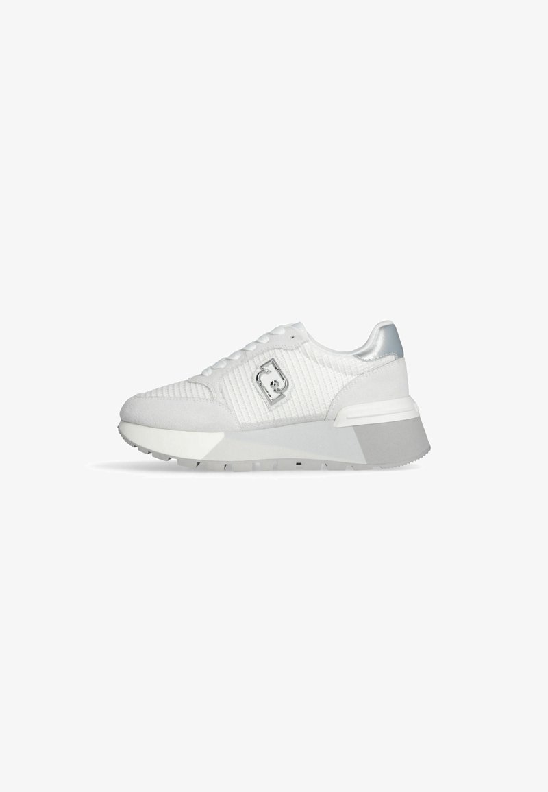 Zapatillas blancas con tela texturizada, un detalle plateado en el talón y una suela gruesa blanca. Presenta un emblema de logo en el lateral.