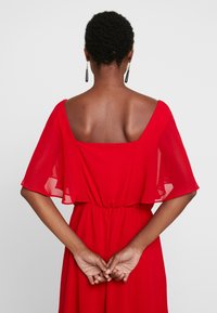 Robe en chiffon rouge avec des manches courtes amples et un dos carré. Taille élastique et jupe fluide, offrant une texture lisse et légère.