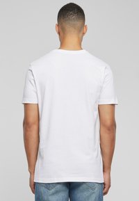 Hvid bomulds t-shirt med korte ærmer og rund hals. Bagfra ses en glat tekstur og et enkelt design. Kombineret med denim jeans.