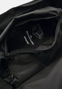 Black duffel bag with a 55L capacity. Made of durable material, featuring a zipper closure and an inside label displaying product details.