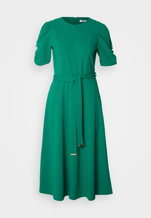 Vestido verde, até ao joelho, feito de um tecido suave. Apresenta mangas curtas e bufantes, uma cintura ajustada com um cinto combinando e um decote redondo.