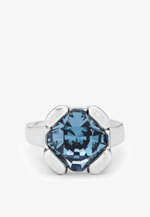 Bague en argent avec une pierre précieuse bleue en forme de hexagone au centre, présentant un design facetté et un contour lisse. Des accents en forme de pétales de fleurs entourent la pierre.