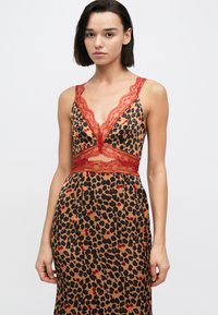 Φόρεμα με λεοπάρ σχέδιο, κόκκινη δαντελωτή λαιμόκοψη σε σχήμα V και λεπτομέρεια στη μέση. Λεία, σατινέ υφή· εφαρμοστή γραμμή που αγκαλιάζει το σώμα με φουσκωτή φούστα.