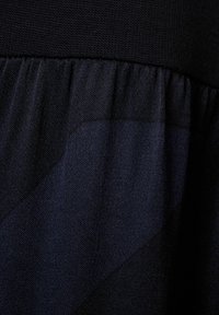 Mörk tyg som kombinerar en solid stickad överdel och en plisserad nederdel med subtila texturvariationer, vilket skapar ett lager-på-lager utseende.