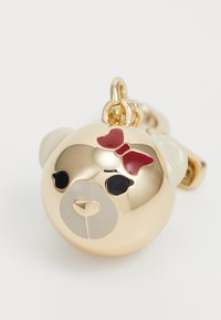 Ciondolo a forma di orso d'oro con un fiocco rosso, occhi neri e un musetto grigio chiaro. Superficie liscia e lucida con un anello di sospensione per il fissaggio.