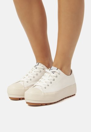 Zapatillas de lona blancas con suela de goma, punta redonda y suela gruesa. Presentan un diseño de cordones y ojales plateados. Suela texturizada para mayor agarre.