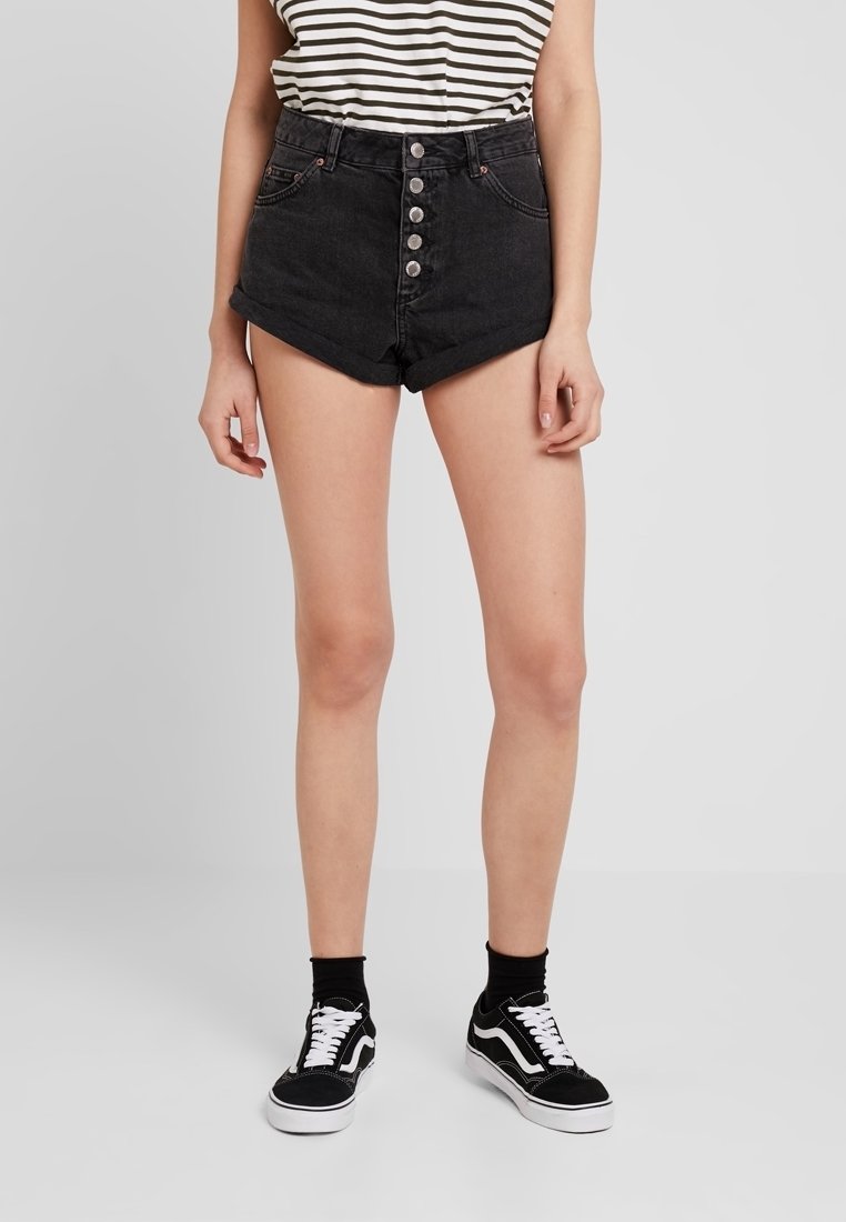 Svarta denimshorts med hög midja, fem knappar som stänger flygningen och framfickor. Kombineras med svarta sneakers och randig top.