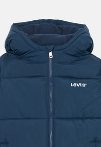 Tamnoplava podstavljena jakna s kapuljačom, prednjim patentnim zatvaračem, flis podlogom i bijelim Levi's logotipom na lijevoj strani prsiju.