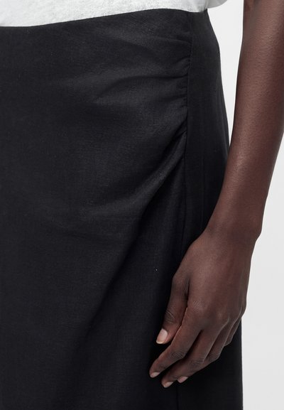 Suurplaan tumejalahast käest, mis puhkab musta rüüga volditud seeliku kõrval, mida kantakse valge pealsega.