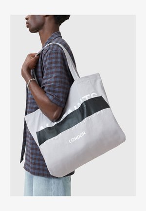 Saco tote cinza em lona com uma faixa preta, com o texto "ALSAINTS" e "LONDRES." Alça de ombro e textura suave.