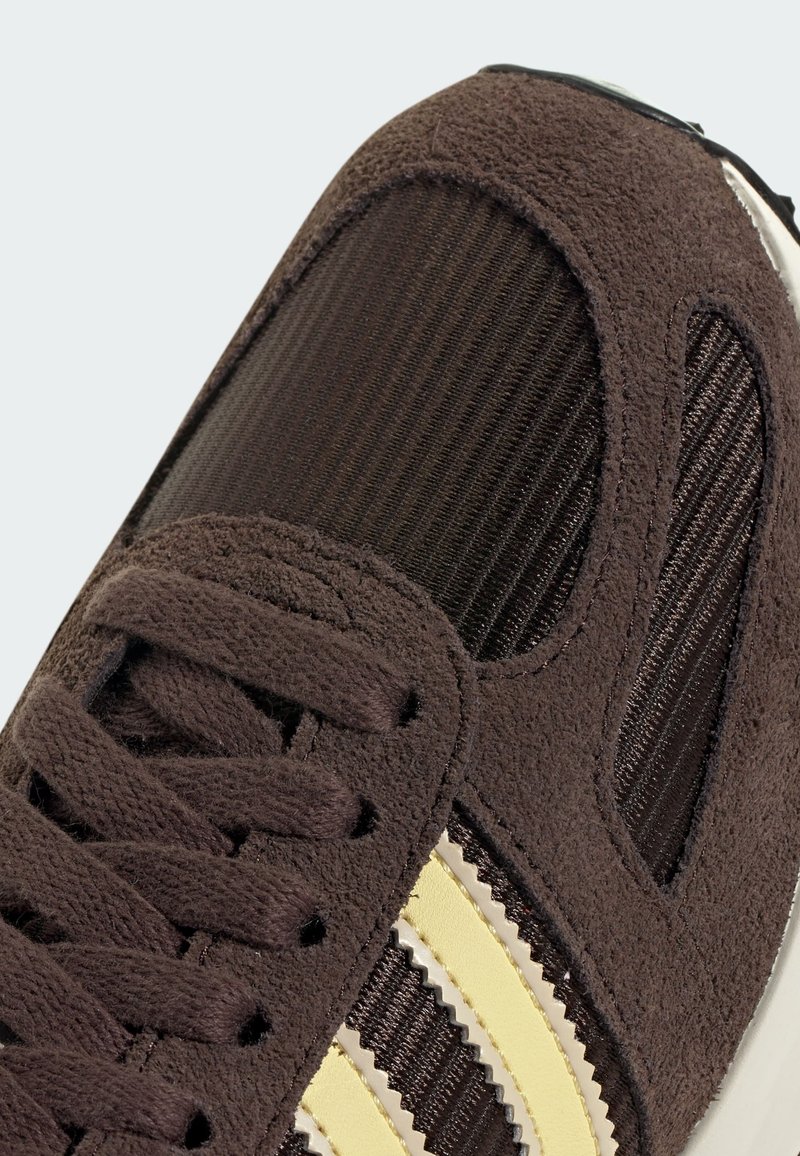 Baskets marron combinant des textures en suède et en mesh. Des bandes jaunes remarquables et des détails de couture complexes améliorent le design.