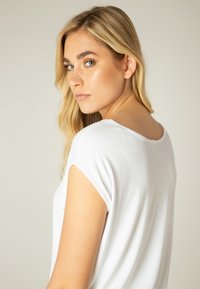 Witte top met korte mouwen, gezien van de achterkant, met een ronde halslijn en een gladde stof, tegen een neutrale achtergrond.