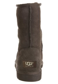 Botín de ante marrón hasta el tobillo con una superficie texturizada, costuras en contraste y un parche rectangular del logo de UGG en el talón.
