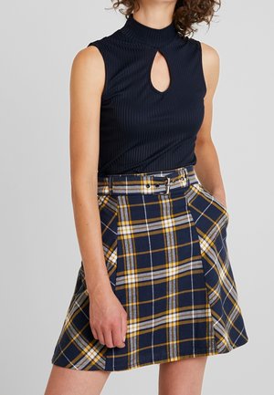 Czarny, bezrękawnik z prążkowanego materiału z dekoltem z kluczykiem, zestawiony z niebieską, żółtą i białą spódnicą w kratę z pasującym paskiem i kieszeniami.