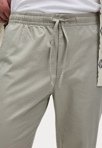 Pantalones jogger de color gris claro, confeccionados en tejido suave, con cintura elástica y cordón, textura lisa y detalles en las costuras laterales.