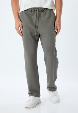 Pantalons à motif gris avec une taille élastique et un cordon de serrage, présentant une coupe décontractée et des poches latérales, associés à des baskets blanches.