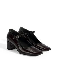 Talons en cuir verni bordeaux brillant avec un bout carré et un talon moyen carré. Présentent une lanière en T avec un accent de boucle en argent.