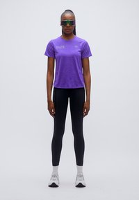 Μωβ αθλητική μπλούζα με κοντά μανίκια, σε συνδυασμό με μαύρα κολάν. Αντιθαμβωτικά γυαλιά ηλίου ολοκληρώνουν την εμφάνιση, τονίζοντας το σπορ στυλ.