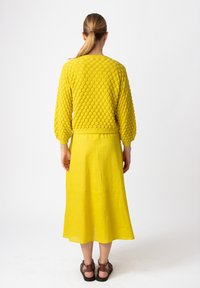 Kollane puff-sleeve sviiter tekstuurse bobble-mustriga ja sobiva pika linase seeliku komplekt. Pruunid rihmadega sandaalid täiendavad komplekti.