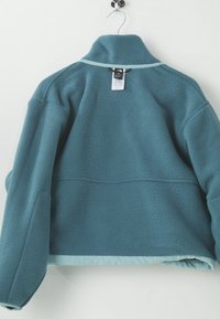 Teal fleece jacket with a high collar and a smooth hem. Features a hanging loop and a tag on the back. Soft texture and relaxed fit.