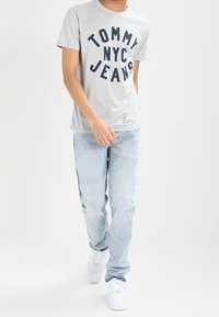 Harmaa lyhythihainen t-paita, jossa on tummansininen "TOMMY NYC JEANS" -teksti, yhdistettynä vaaleansinisiin farkkushortseihin ja valkoisiin lenkkereihin.
