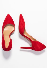 Escarpins en daim rouge avec un bout pointu et des côtés ouverts, dotés d'un talon aiguille fin et d'un intérieur beige. Sans motifs ni accents visibles.