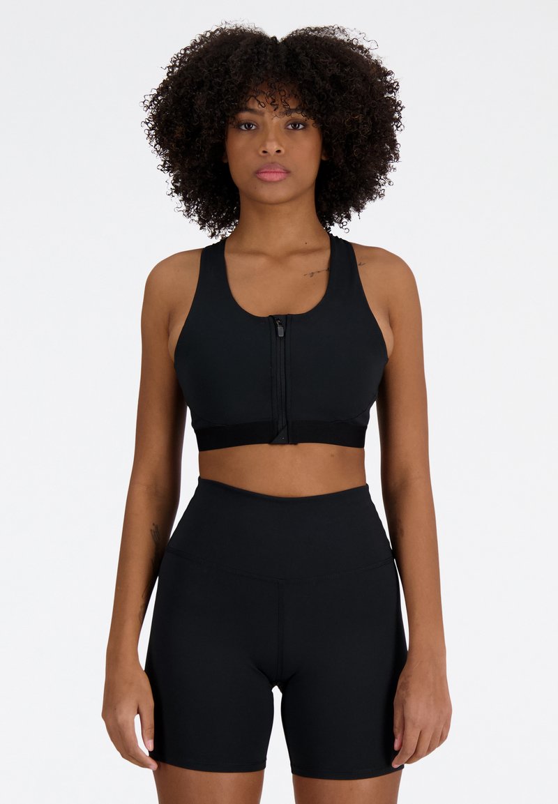 Soutien-gorge de sport noir avec une fermeture éclair à l'avant et des bretelles larges, associé à un short noir taille haute. Les deux articles sont en tissu lisse et extensible.