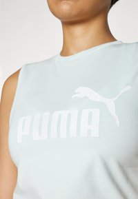 Svijetloplava bezrukavna sportska majica izrađena od glatkog materijala sadrži veliki bijeli "PUMA" logo i bijelu grafiku skakačke mačke.