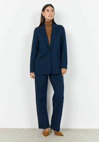 Abito sartoriale blu navy con giacca a un bottone e pantaloni dritti, realizzato in tessuto morbido, abbinato a un dolcevita marrone.