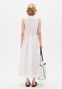 Abito bianco senza maniche con vita arricciata, lunghezza al di sotto del ginocchio e cuciture decorative all'orlo. Abbinato a una borsa a tracolla bianca.