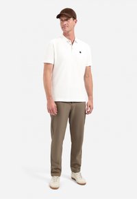 Witte poloshirt met een kraag, bruine pet, olijfgroene broek en witte schoenen. De outfit heeft een minimalistisch ontwerp zonder zichtbare patronen.