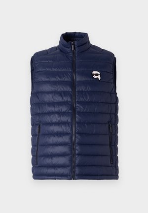 Navyblauwe gewatteerde vest met een hoge kraag, rits aan de voorkant en zijzakken. Heeft een horizontaal gestikt ontwerp en een klein logo detail.