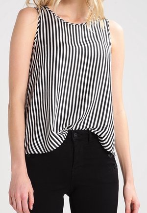 Kvinde iført en ærmeløs top med sorte og hvide lodrette striber, let stoppet ned i højtaljede sorte bukser.