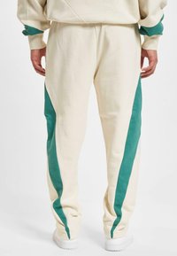Kremfargede joggebukser med teal sidepaneler, laget av myk Stoff. Har en innsvingt design og elastisk midjebånd.