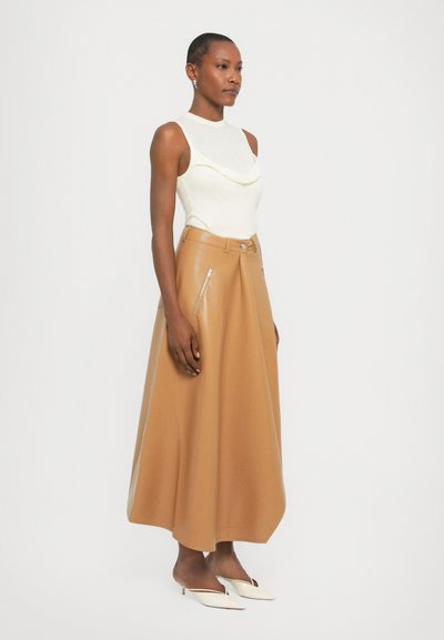 Cowl-neck crème top gecombineerd met een lange, tan leren rok met zijritsen, een gladde textuur en een uitlopende silhoët. Witte hoge muiltjes.