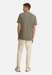 Olivengrøn kort�ærmet t-shirt med rund hals, iført med lyse bukser og beige sneakers, set bagfra.
