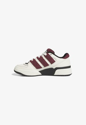 Der Sneaker besteht aus weißem synthetischem Leder mit bordeauxroten Wildlederstreifen, schwarzen Akzenten, einer strukturierten schwarzen Gummisohle und weißen Schnürsenkeln.