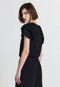 T-shirt nera a maniche corte, caratterizzata da dettagli in rilievo e frange sulle spalle. Tessuto morbido, vestibilità comoda e design semplice.