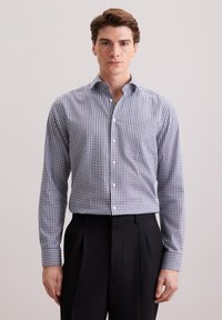 Camicia a quadri con colletto allargato, motivo gingham blu e bianco, maniche lunghe e chiusura con bottoni; abbinata a pantaloni neri plissettati.