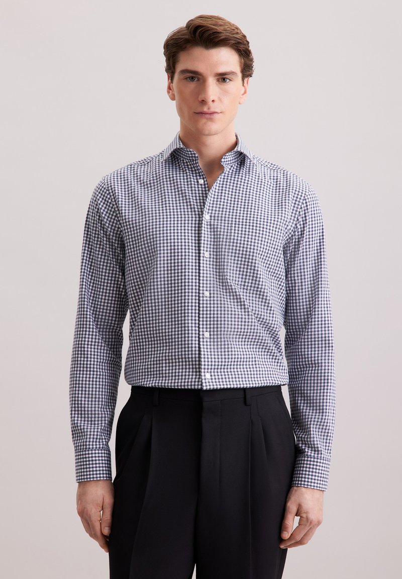 Camicia a quadri con colletto allargato, motivo gingham blu e bianco, maniche lunghe e chiusura con bottoni; abbinata a pantaloni neri plissettati.