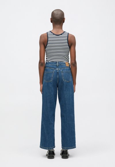 Stripet tanktop med vide blå denim jeans som har høy midje, distinkte baklommer og et lærmerke på livet.