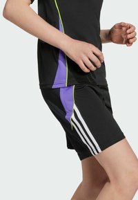 Top atletico nero e pantaloni corti con accenti viola e verde, con tre strisce bianche sul lato dei pantaloni. Realizzato in materiale traspirante.