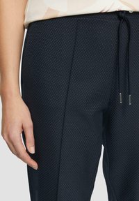 Pantalons bleu marine avec un motif de pois subtil, dotés d'une taille à cordon de serrage, d'une texture lisse et d'une coupe ajustée.