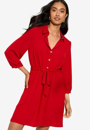 Red dress with a collared neckline, button front, and tie waist. Long sleeves gather at the wrists, made from a smooth, lightweight fabric.