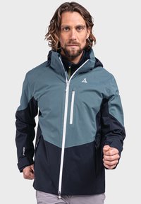 Wasserdichte Jacke in Türkis und Marineblau, mit einem geometrischen Design, verstellbarem Kapuzenkragen, Frontreißverschluss und zwei Seitentaschen.