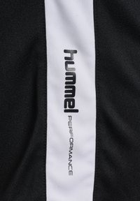 Zwart sportstof met een verticale witte streep waarop "hummel" in vetgedrukte zwarte letters staat en "PERFORMANCE" in kleinere grijze tekst.